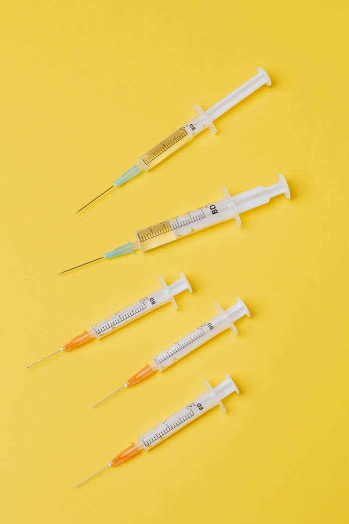 Top view arrangement of medical single use syringes with vaccine and small empty syringes without needle cover placed on yellow surface